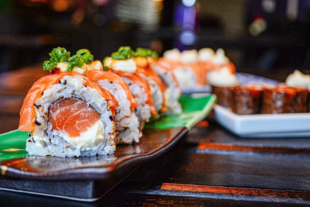 Salmon and cream cheese sushi rolls with green onions on a dark plate.