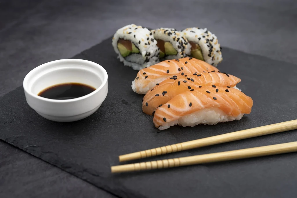 Salmon nigiri, maki rolls, soy sauce, and chopsticks on dark slate.