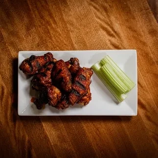 Top-down: Charred chicken wings and celery sticks on a white plate.