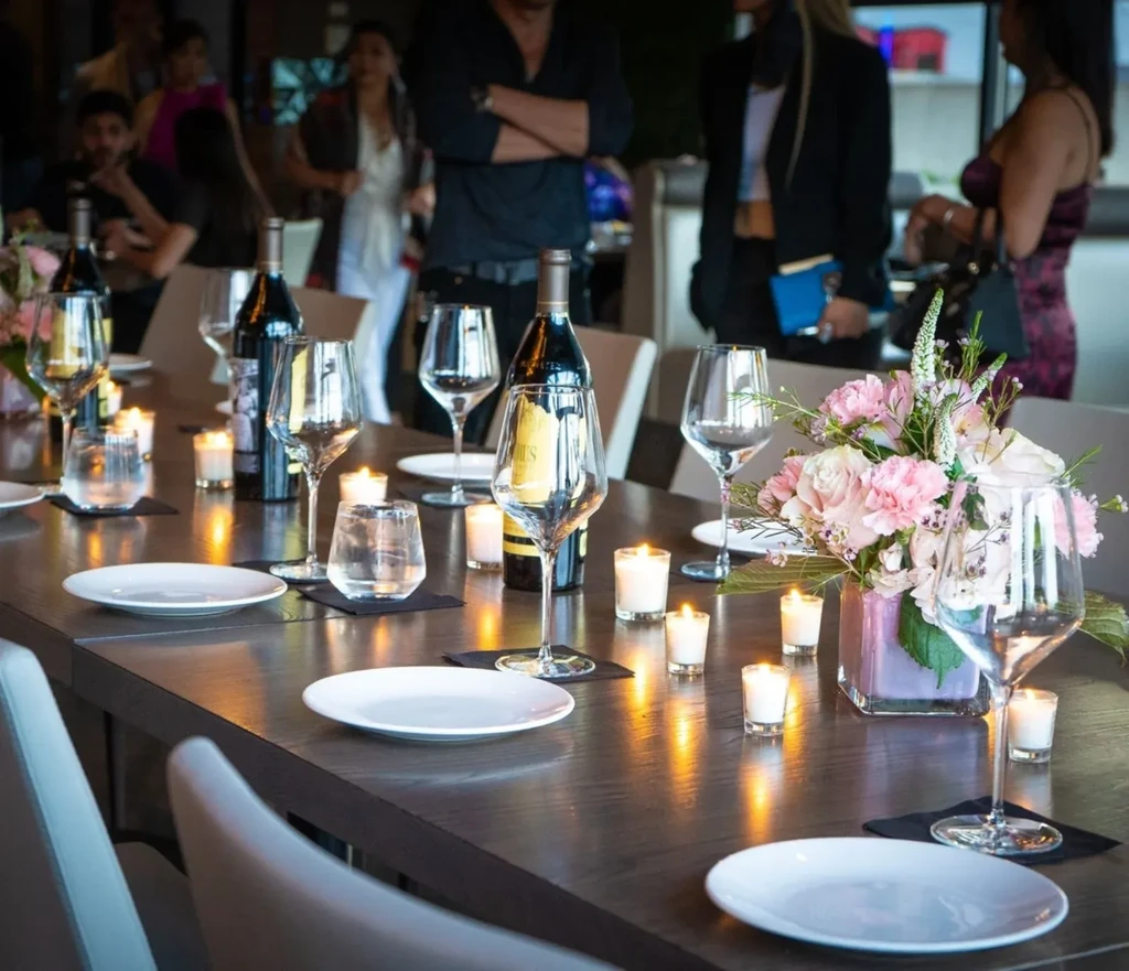 Dining table set with wine bottles, glasses, pink flowers, and lit candles.