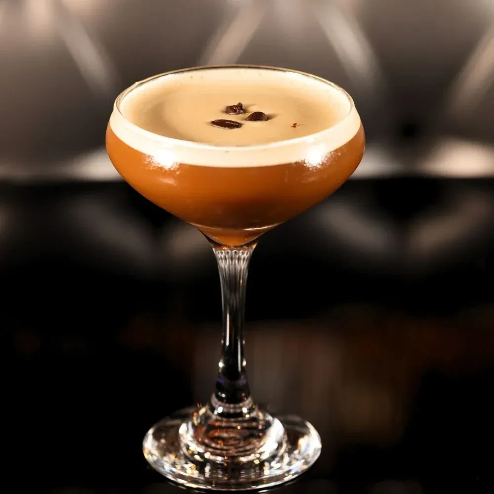 Amber cocktail in coupe glass, with creamy foam and three coffee beans.
