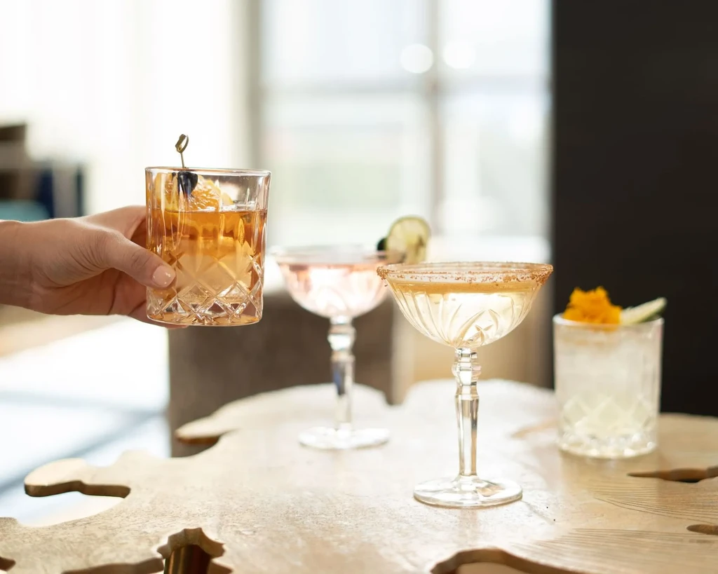 Four distinct cocktails on organic wooden table, one held by hand.