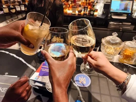 Three diverse hands clinking cocktails and wine in a toast.