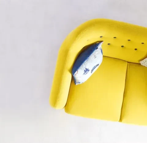 Overhead view of a bright yellow rounded sofa and nautical pillow.