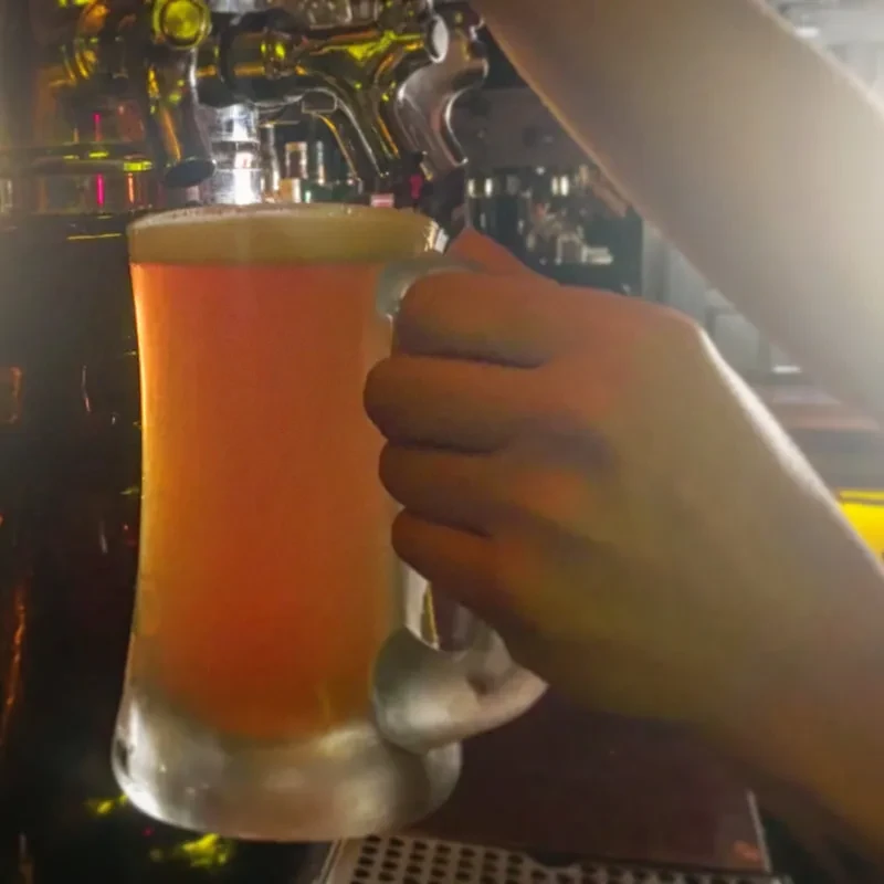 A hand fills a foamy beer mug from a bar tap.