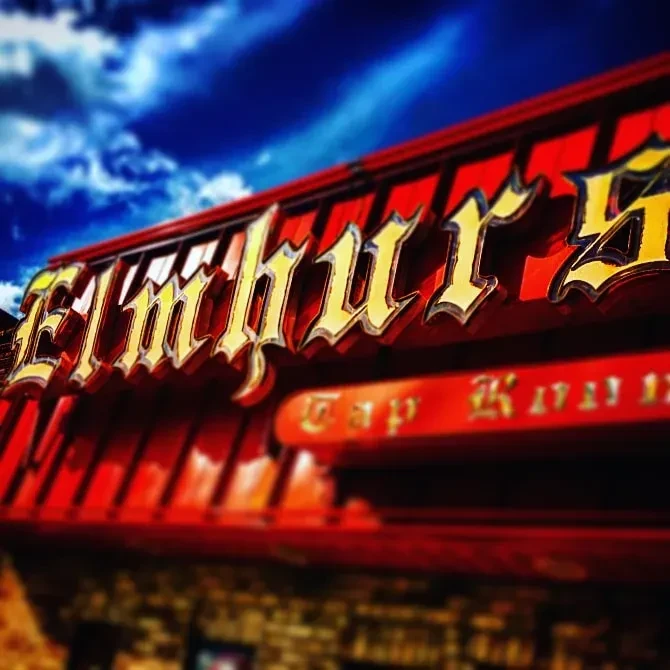 Golden Elmhurst Tap House sign on a red roof against blue sky.