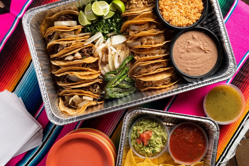 Overhead: Mexican food catering with tacos, sides, and salsas on a serape.