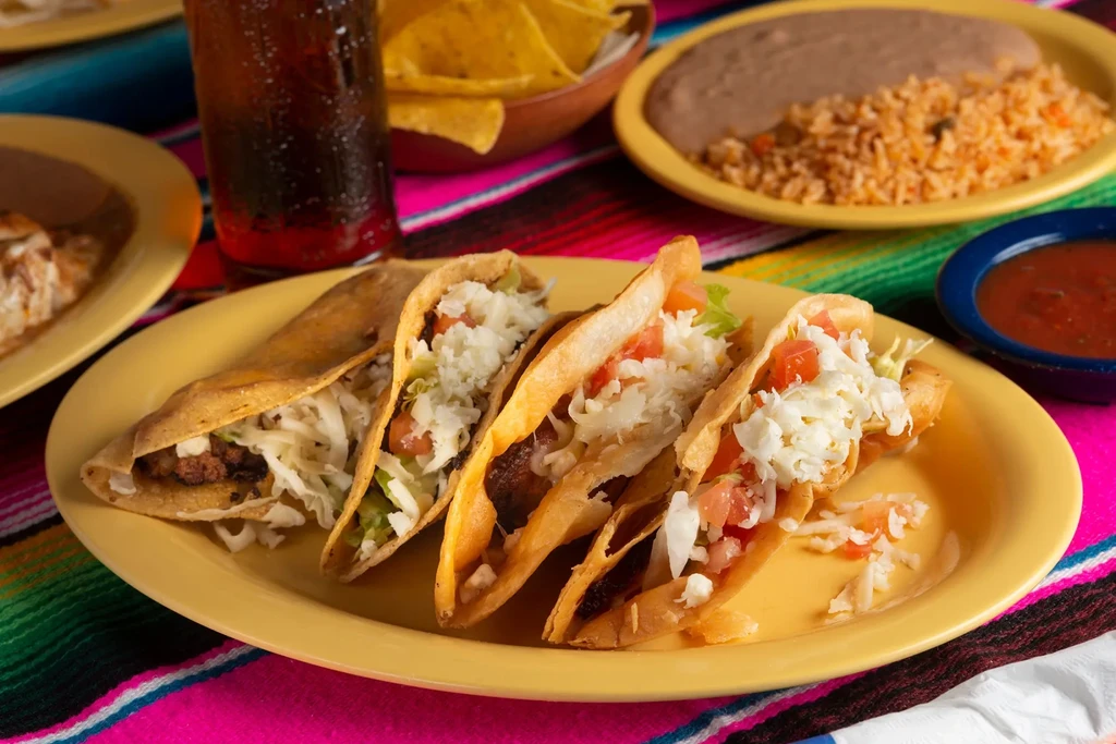 Four hard-shell Mexican tacos with rice, beans, and red salsa.