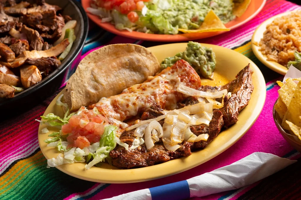 Grilled meat, enchilada, guacamole, rice, chips on a colorful serape.