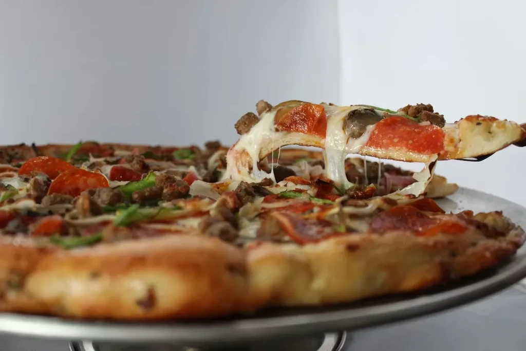 Pizza slice lifted, revealing melted cheese, pepperoni, and bell peppers.