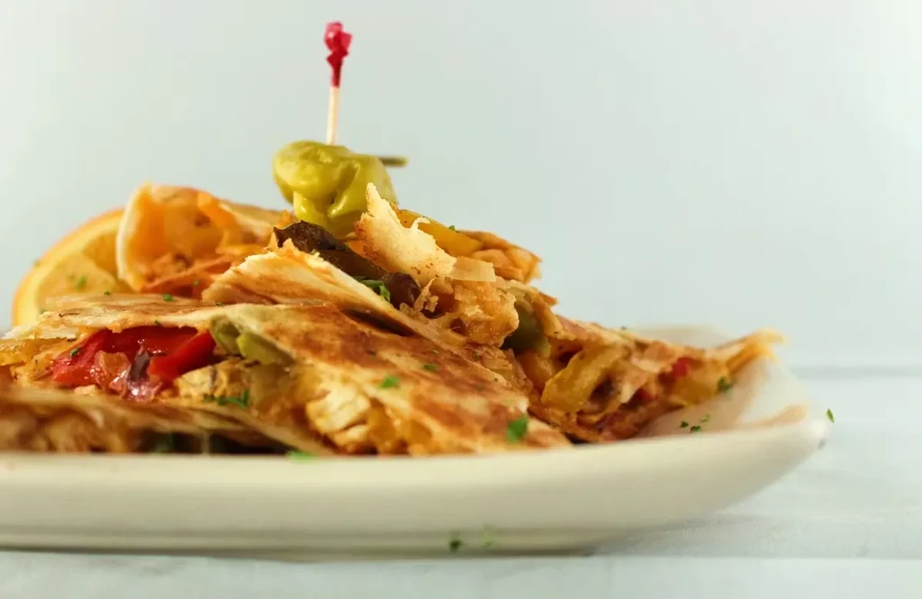 Golden-brown chicken quesadilla wedges with peppers, herbs, and a pepperoncini.
