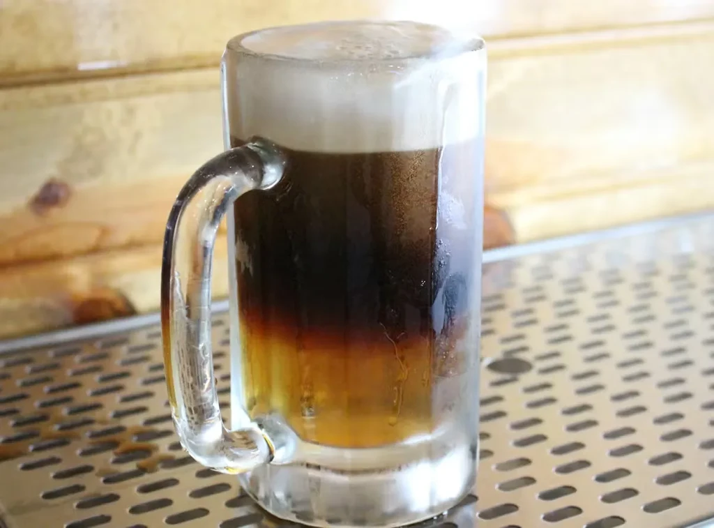 Frosty layered drink in a glass mug on a bar tray.