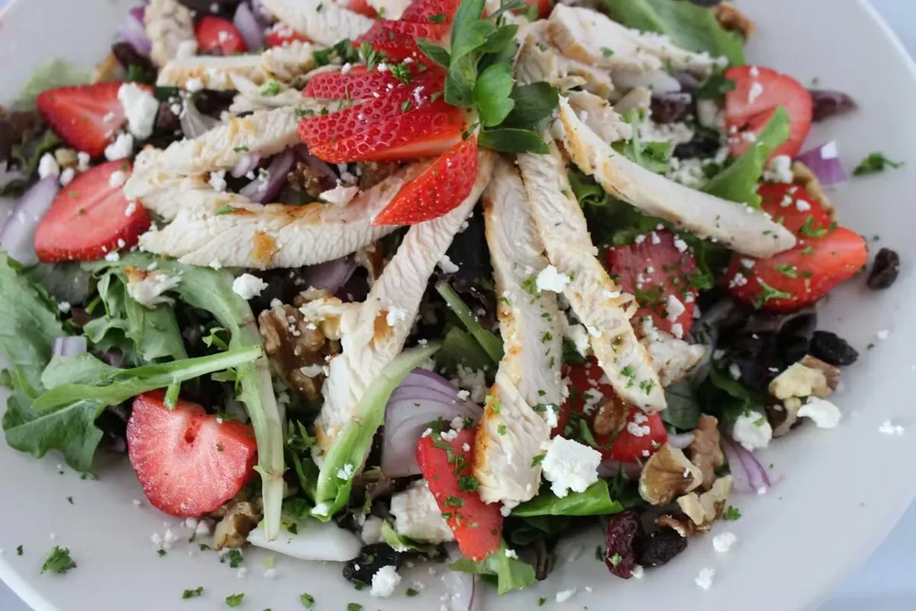 Grilled chicken, strawberry, cheese, and walnut salad on a plate.