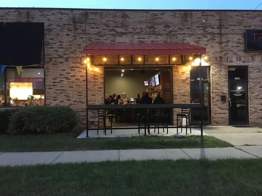 Brick restaurant exterior at dusk with open entrance, red awning, string lights.