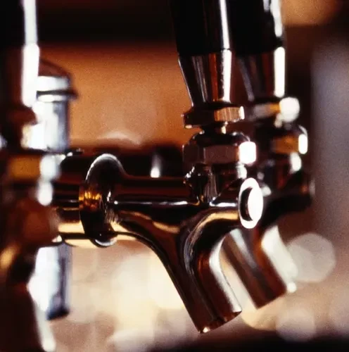 Close-up of several chrome beer taps in a row at a dimly lit bar.
