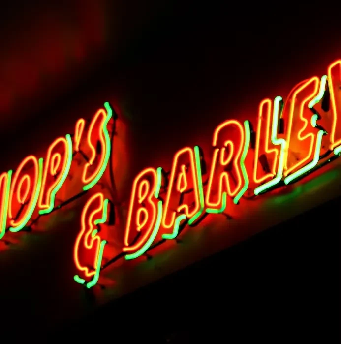Glowing orange and green neon sign "HOP'S & BARLEY" on dark background.