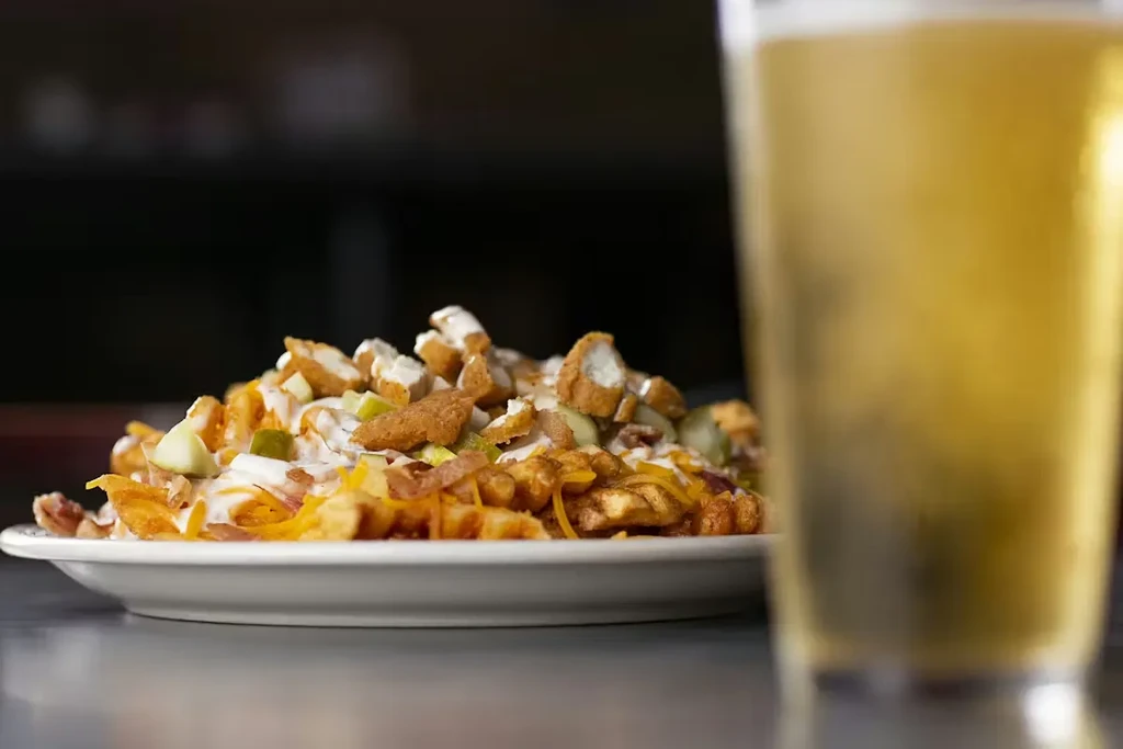 Loaded fries topped with chicken, cheese, and sauce, next to a beer.