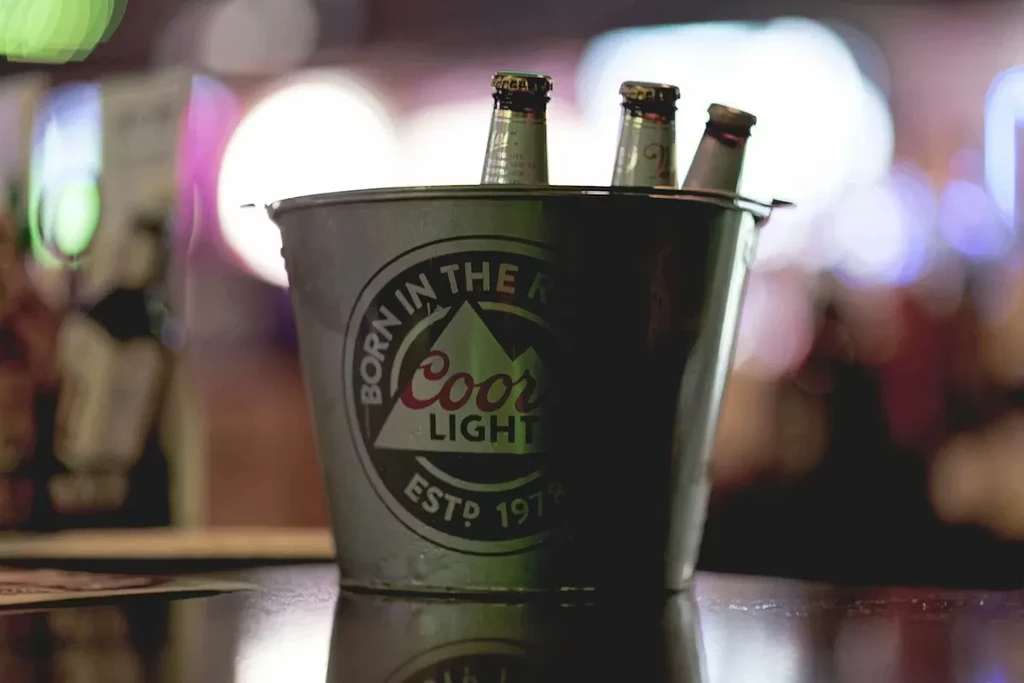 A Coors Light ice bucket holds three beers on a dark bar.