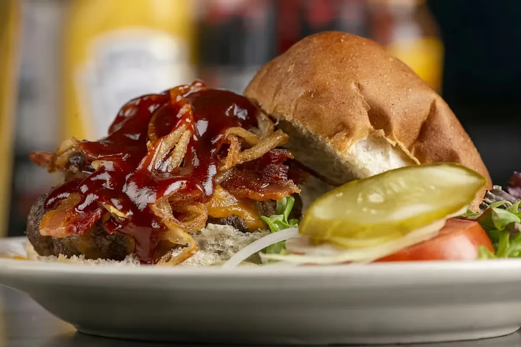 Close-up of an open burger with crispy onions, bacon, and pickle.