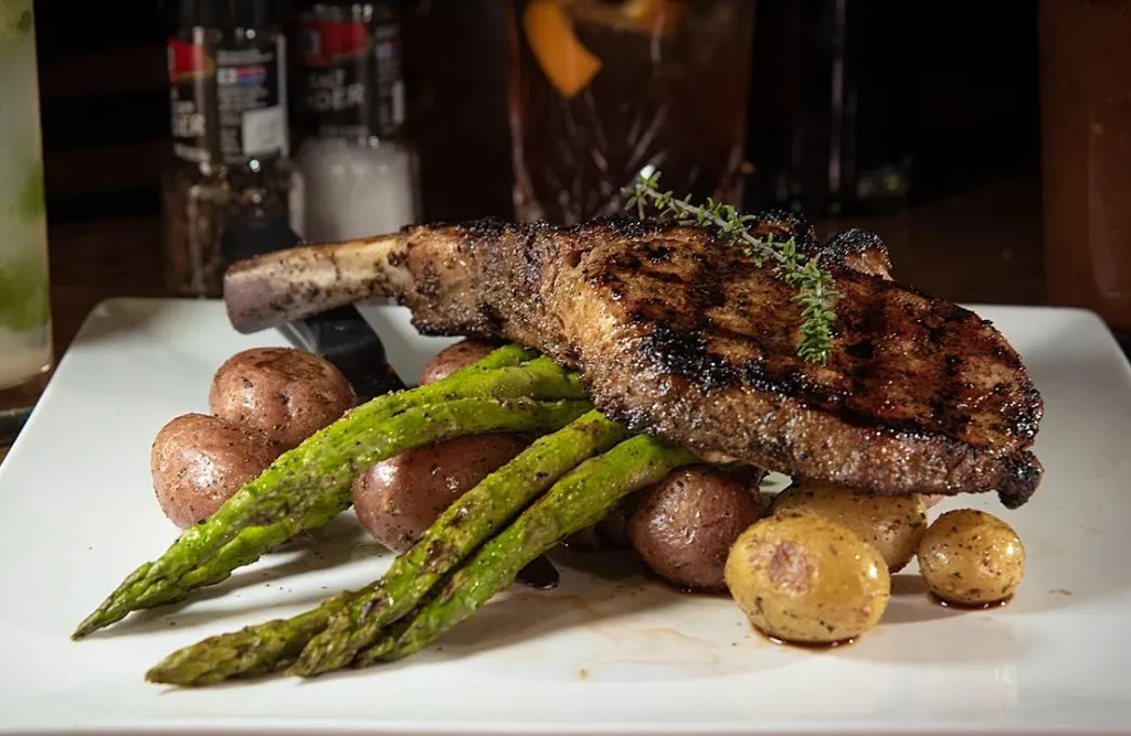 Seared tomahawk steak, asparagus, and baby potatoes on a white plate.
