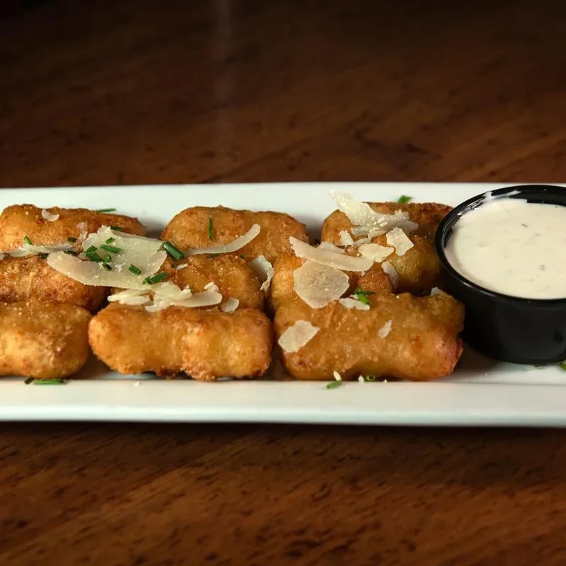 Close-up of fried cheese curds with Parmesan, chives, and creamy dipping sauce.