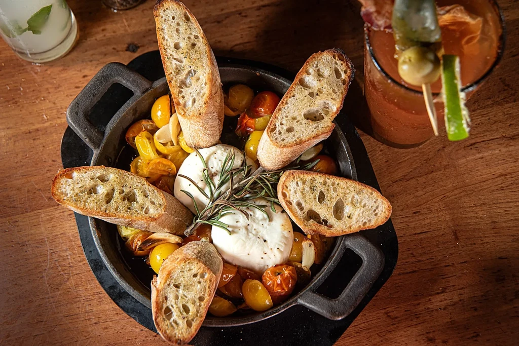 Creamy cheese, roasted tomatoes, garlic, and bread in a cast-iron pan.