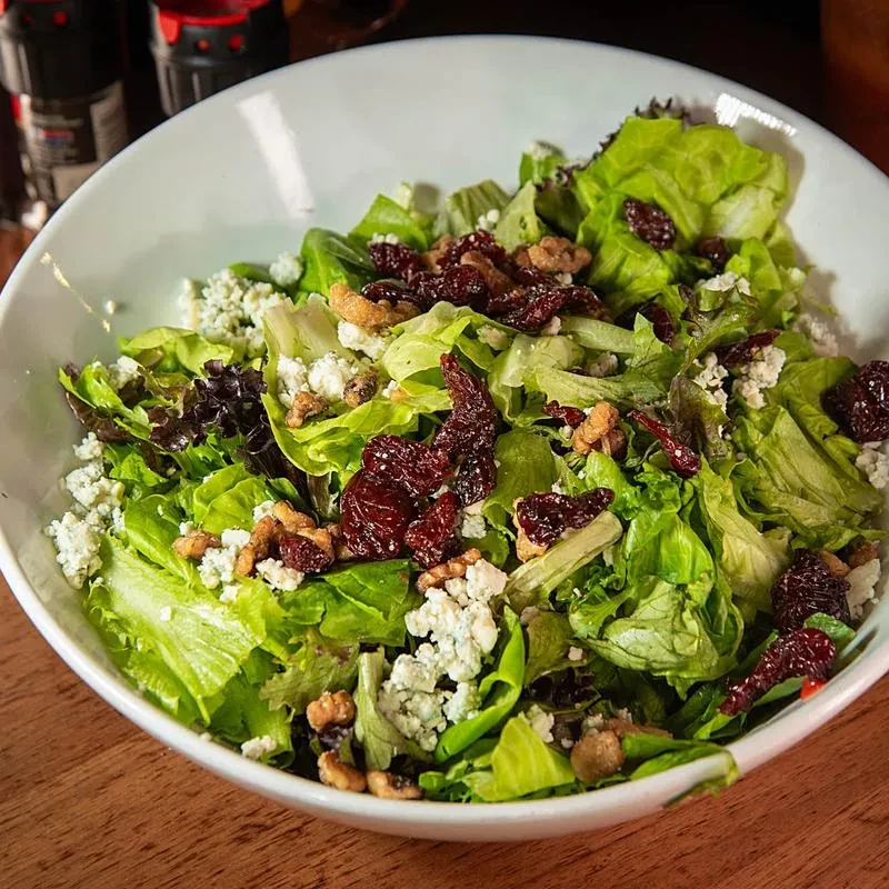 Fresh salad in white bowl with lettuce, blue cheese, cranberries, walnuts.