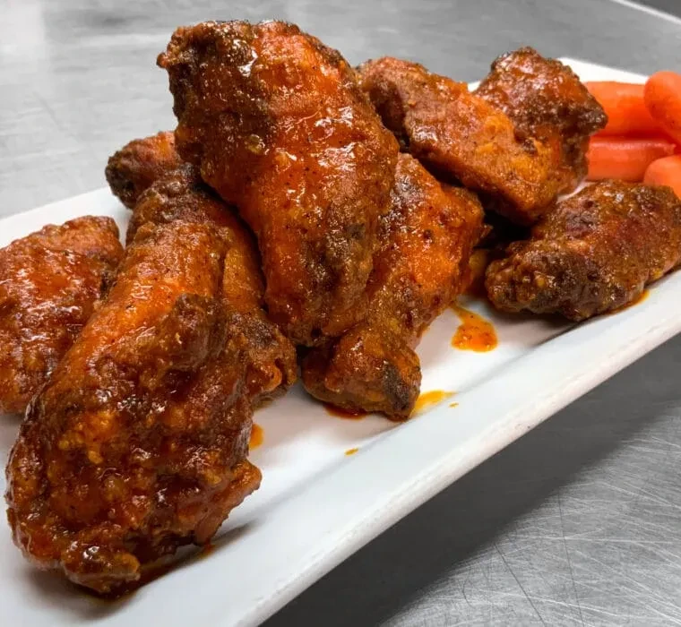 Glossy, reddish-orange chicken wings with carrots on a white plate.