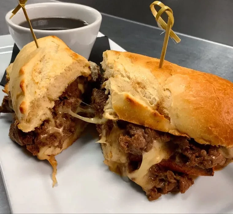 Beef and melted cheese sandwich, cut in half, on a white plate.