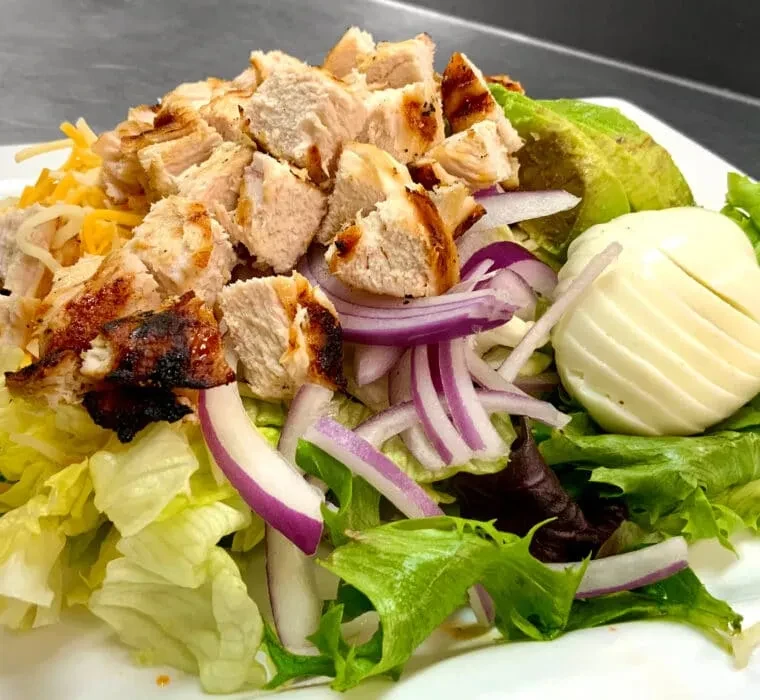 Mixed green salad with grilled chicken, avocado, red onion, and egg.