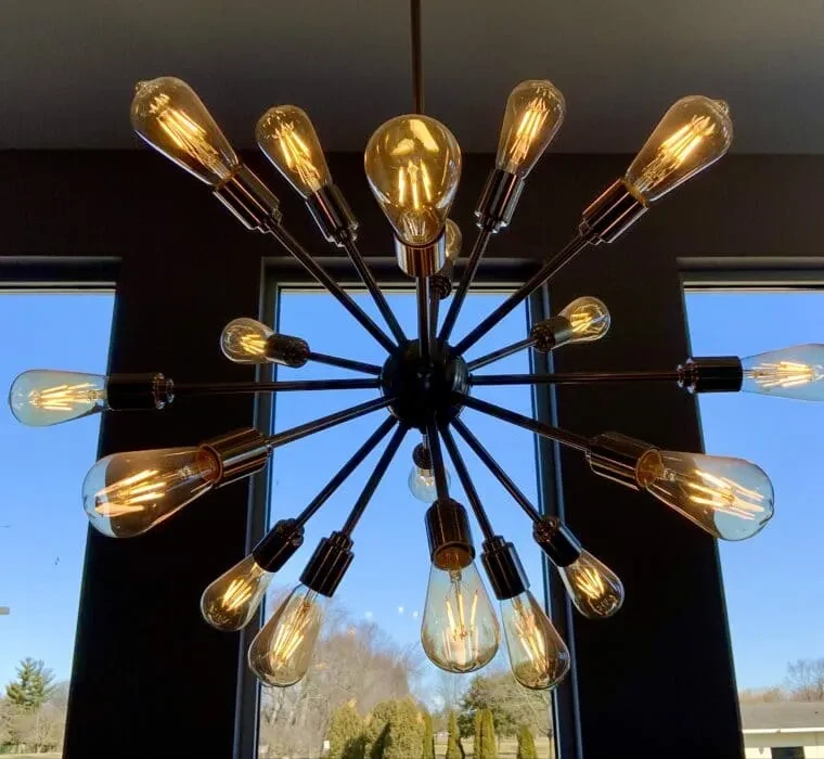 Dark sputnik chandelier with many amber-glowing Edison filament bulbs.