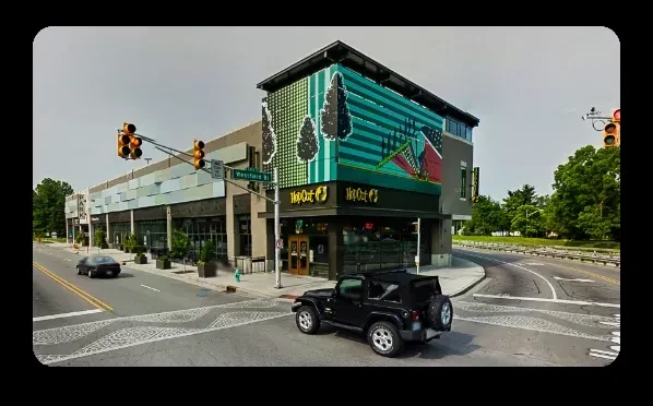 Modern building with "Hop Out" restaurant and green mural at sunny intersection.
