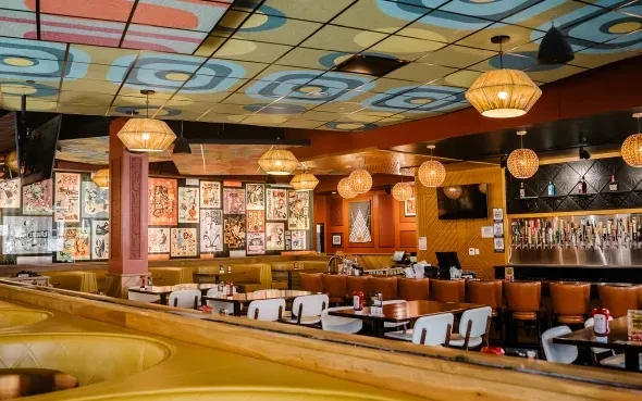Eclectic restaurant interior with colorful geometric ceiling, art collage, and bar.