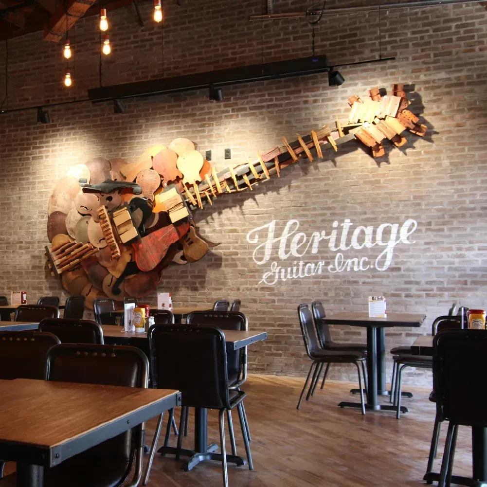 Deconstructed guitar sculpture on brick wall next to 'Heritage Guitar Inc.' text.