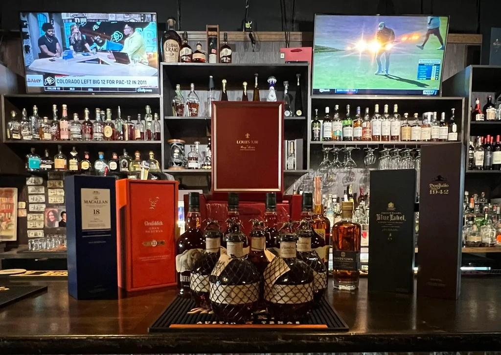 Premium liquor bottles displayed in a high-end bar with TVs showing sports.