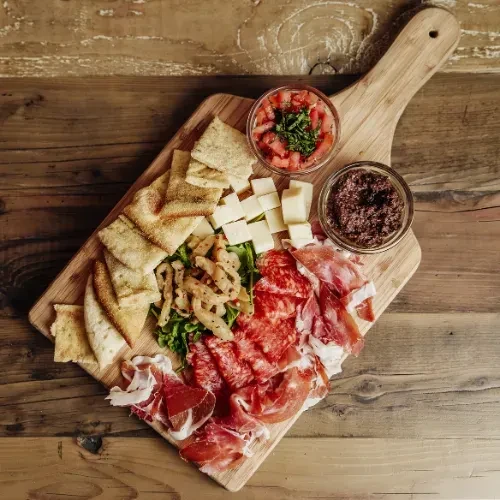 Rustic wooden charcuterie board with meats, cheese, flatbread, salsa, and tapenade.