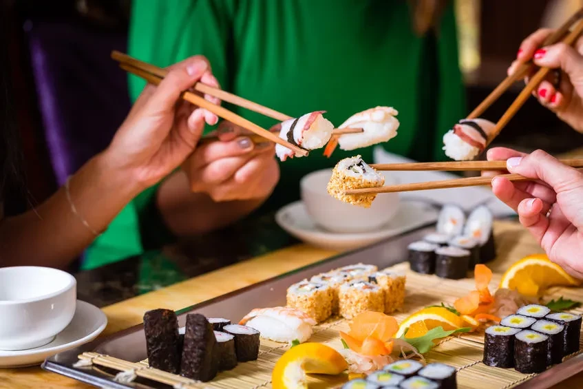 Hands with chopsticks selecting sushi from a vibrant platter.