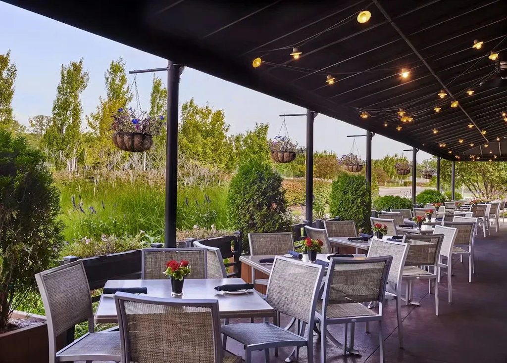 Restaurant patio with set tables, flowers, string lights, and lake view.