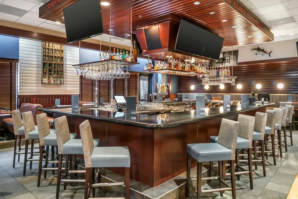 Modern U-shaped bar, dark wood, black counter, stools, and liquor bottles.