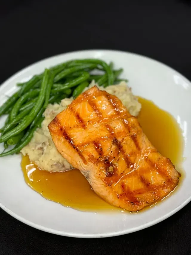 Amber-glazed salmon, rustic mashed potatoes, and green beans on a plate.