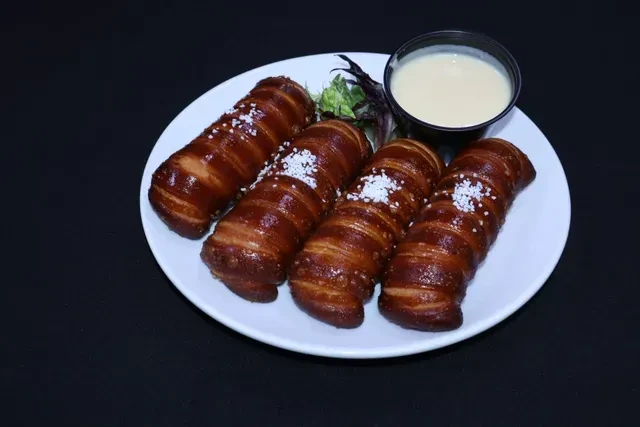 Four salted baked pretzels with dipping sauce and lettuce on a plate.
