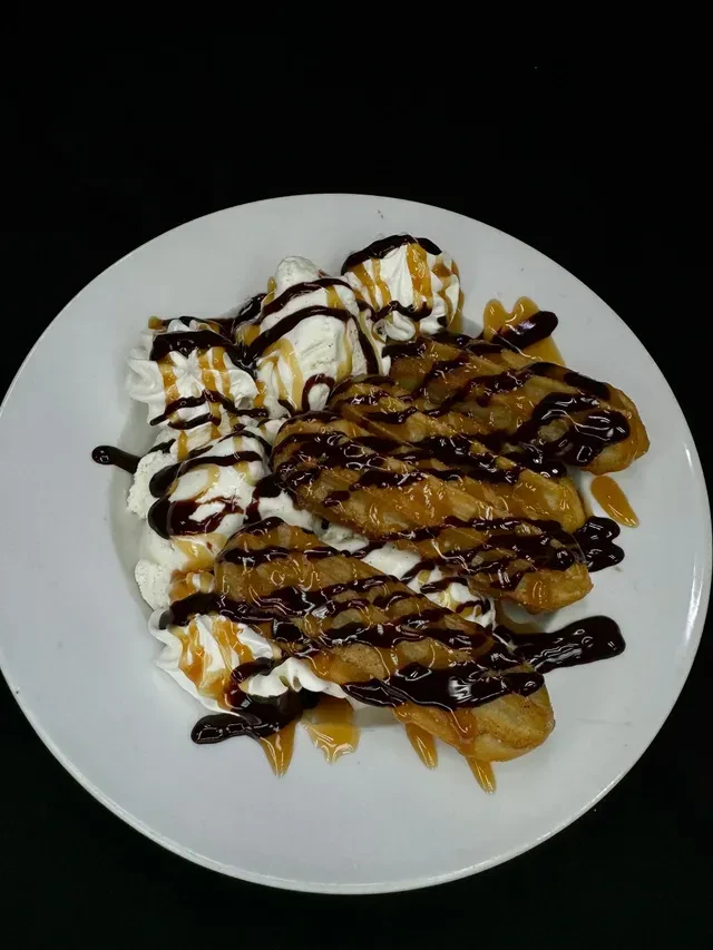 Golden-brown churros topped with ice cream, chocolate, and caramel sauces.