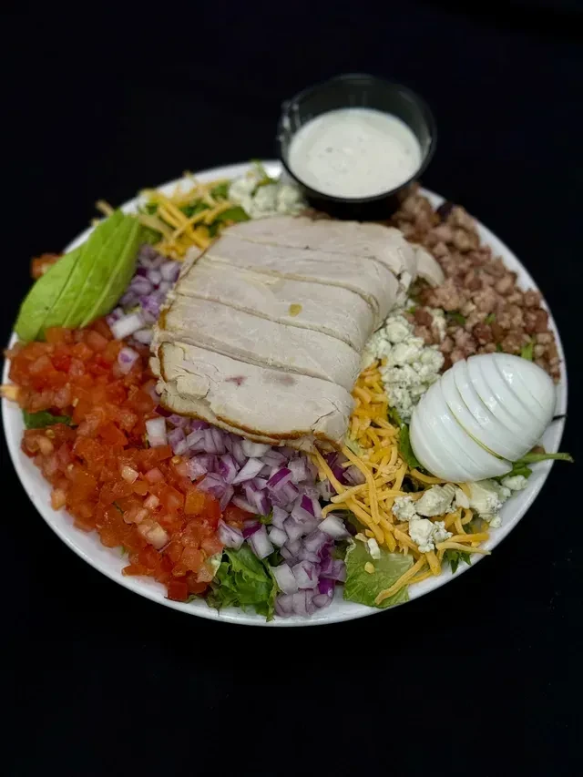 Colorful Cobb-style salad with turkey, egg, avocado, cheeses, and dressing.