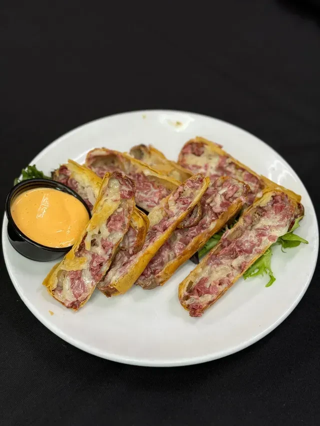 Plate of golden-brown fried corned beef and cheese rolls with sauce.
