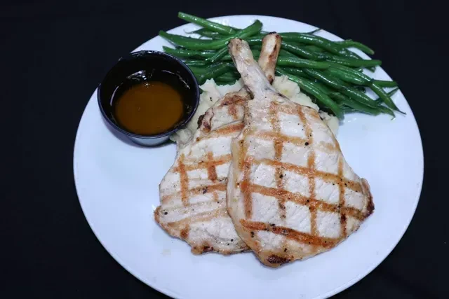 Two grilled pork chops with mashed potatoes, green beans, and gravy.