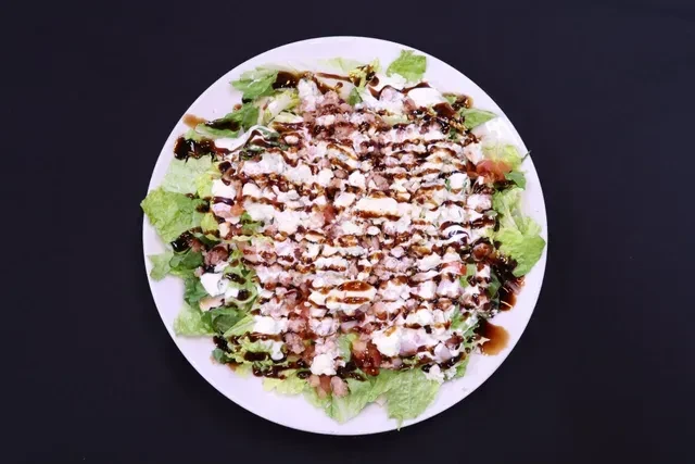 Overhead: gourmet green salad with cheese, red bits, and two drizzles.