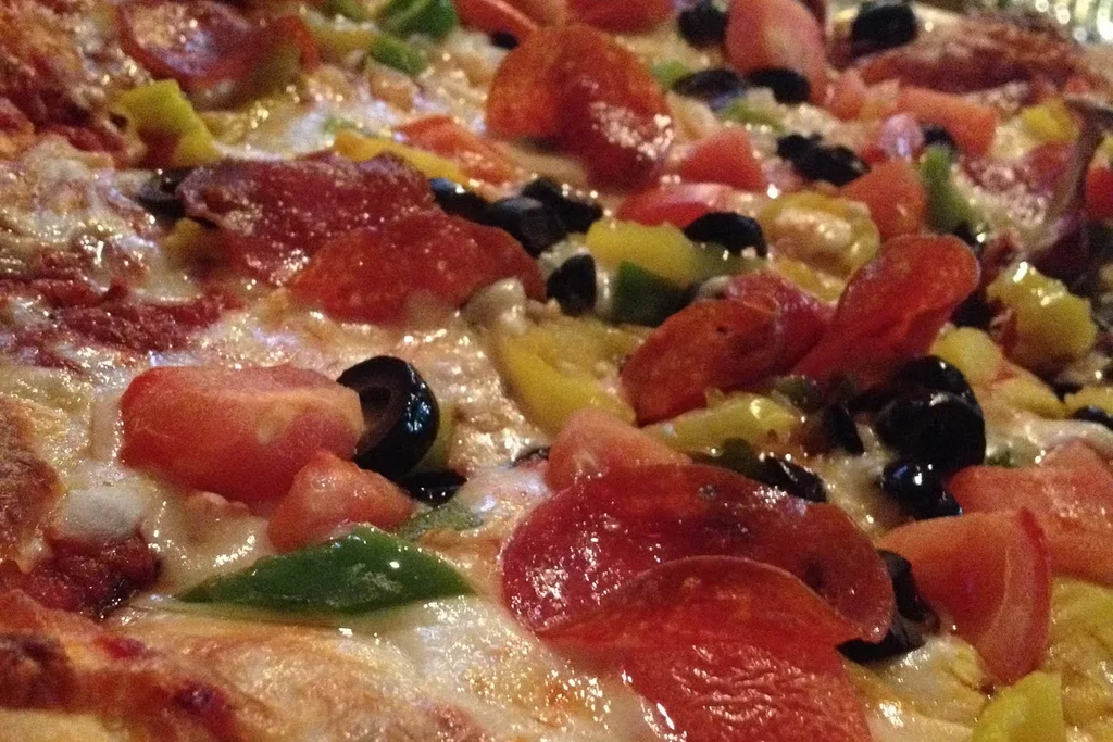Top-down close-up of pizza with pepperoni, olives, tomatoes, and peppers.