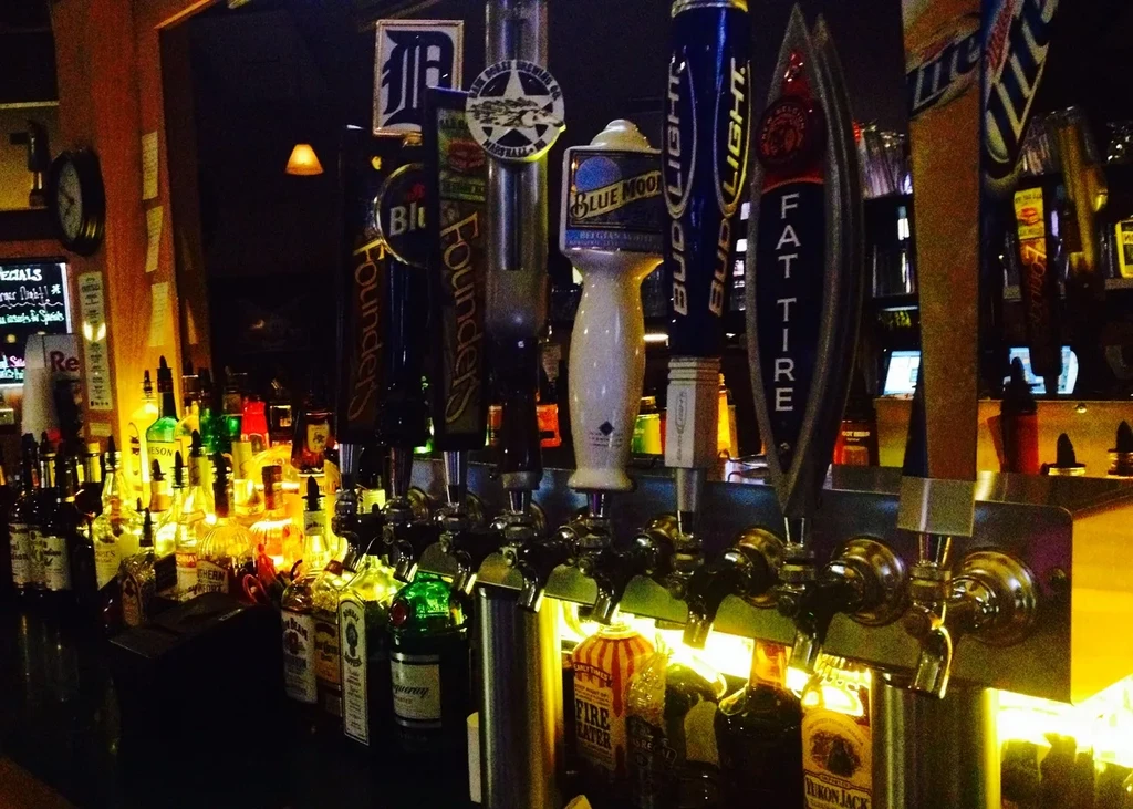 Dimly lit bar counter with glowing liquor bottles and prominent beer taps.
