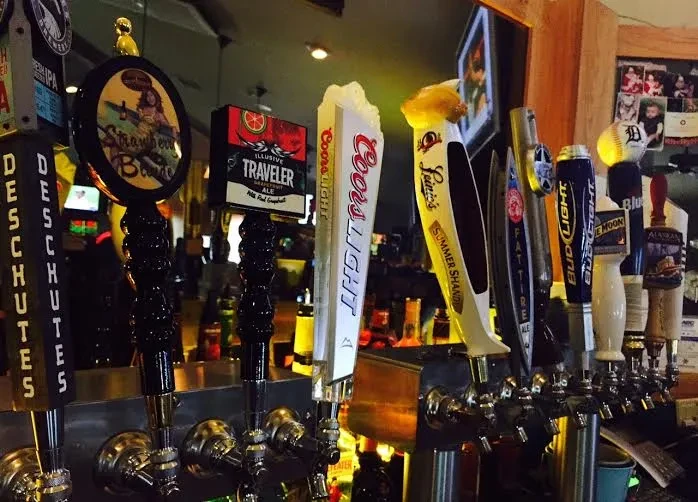 Row of diverse beer tap handles showing brand names at a bar.