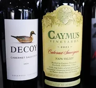 Two wine bottles, Decoy and Caymus Cabernet Sauvignon, with distinct labels.